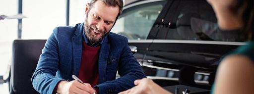 man sitting at desk filling out car purchase paperwork