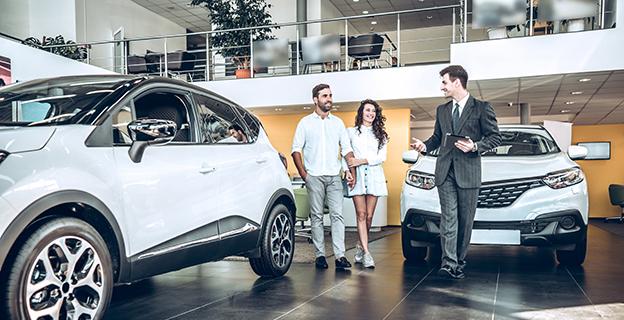 A couple talks to a salesperson in a car showroom.