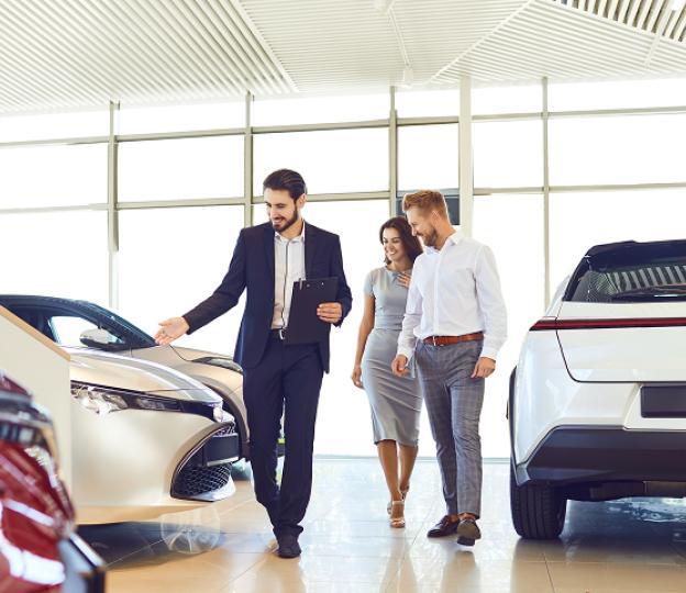 sales person showing man and woman around car dealership
